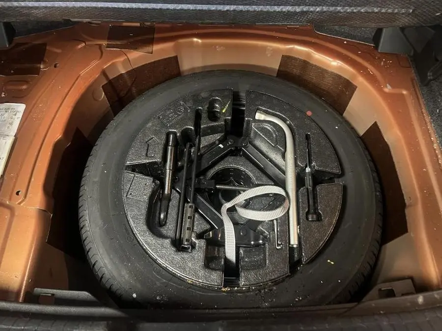 Vue rapprochée de la roue de secours noire et des outils de bord dans le coffre orange de la Volkswagen Polo 2019.