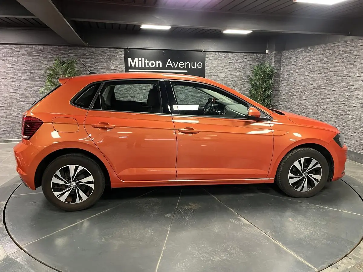 Profil droit d'une Volkswagen Polo orange métallisée 2019 avec jantes alliage et rétroviseurs couleur carrosserie.