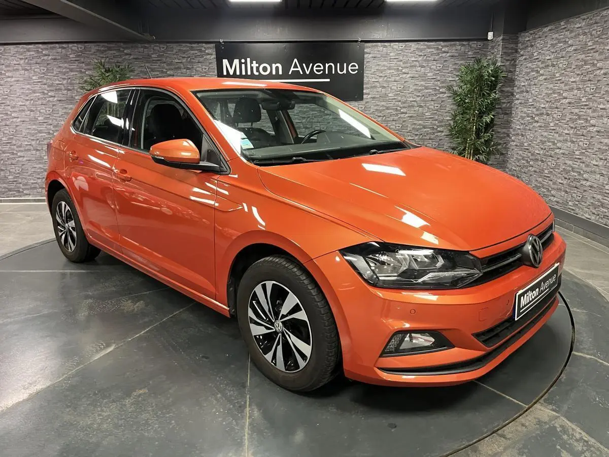 Volkswagen Polo orange vue 3/4 avant droit, jantes alliage bicolores et calandre avec logo VW visible