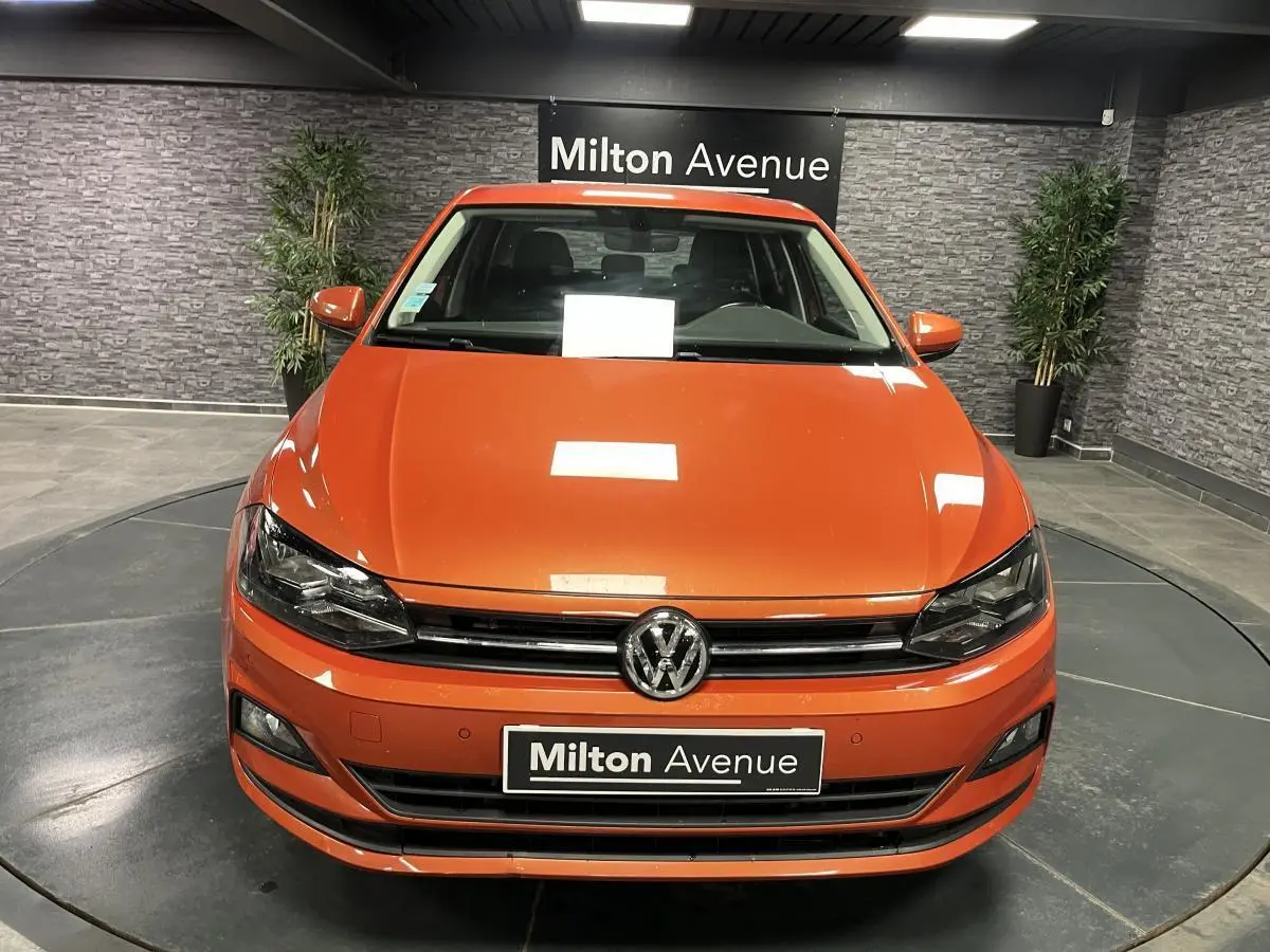 Vue frontale d'une Volkswagen Polo orange métallisée 2019 avec calandre chromée et plaque Milton Avenue.