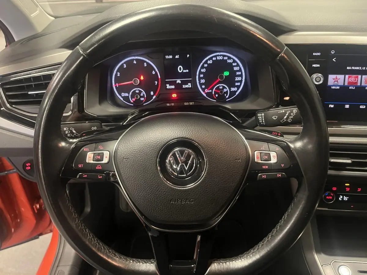 Vue intérieure centrée sur le volant cuir multifonction de la Volkswagen Polo orange avec tableau de bord numérique.
