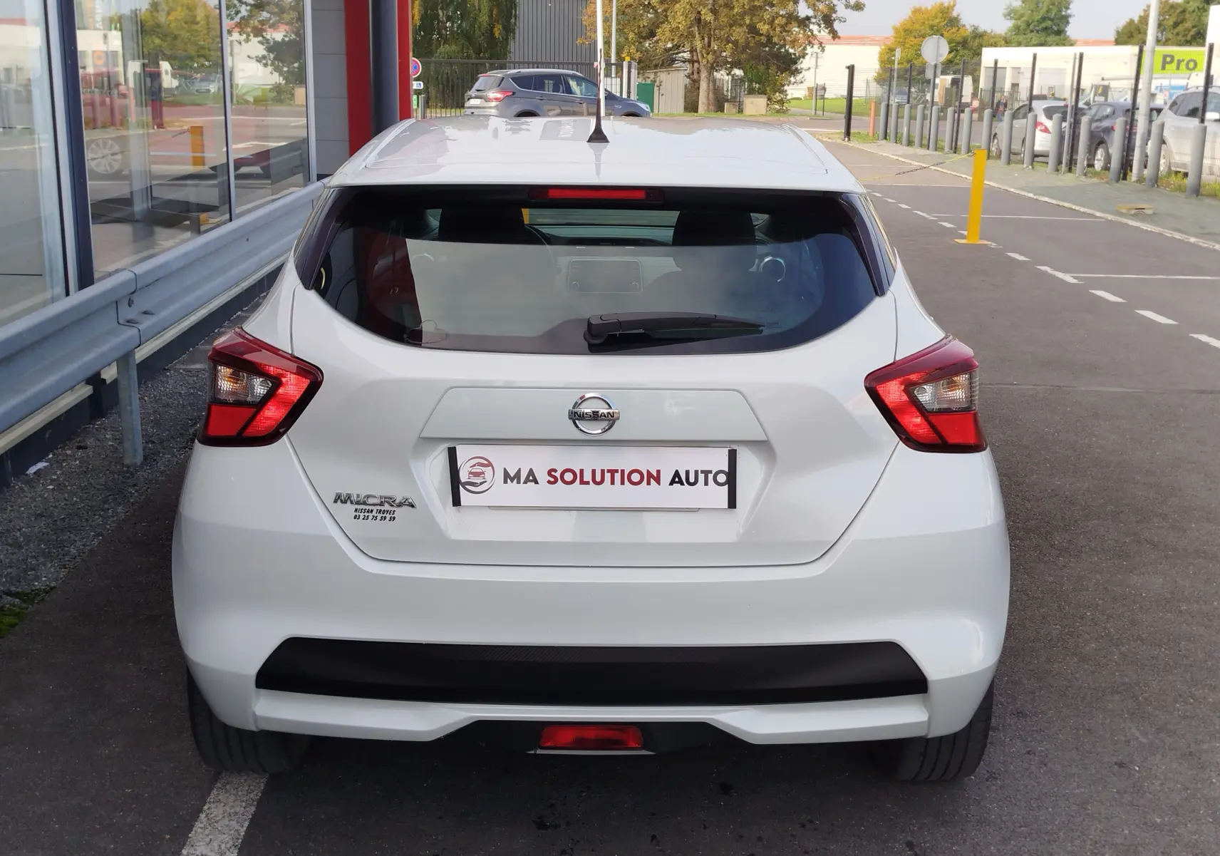 Vue arrière d'une Nissan Micra blanche 2019 avec feux arrière anguleux et logo visible sur parking.