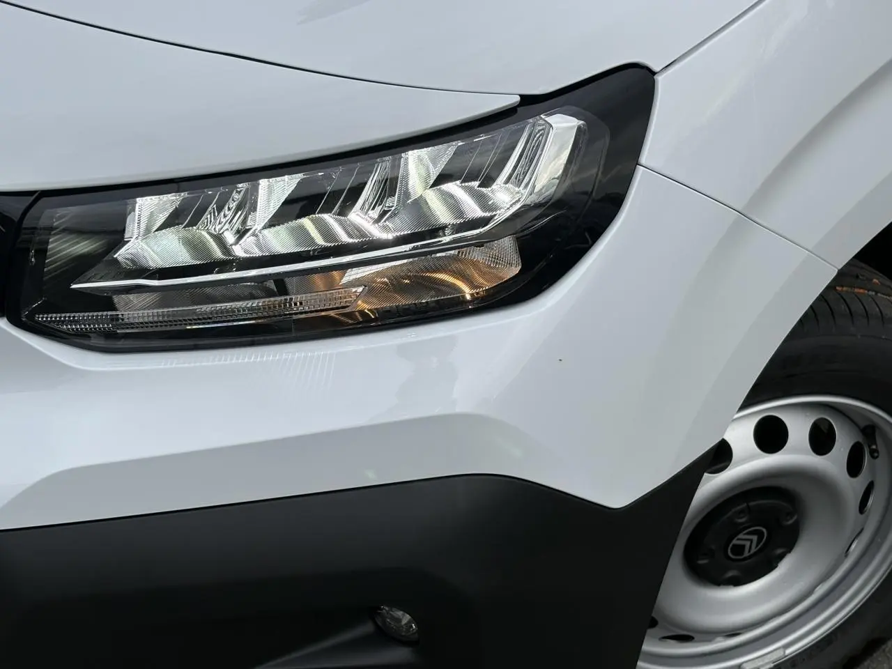 Gros plan sur le phare avant droit et la roue tôle grise du Citroën Berlingo blanc Icy 2025.