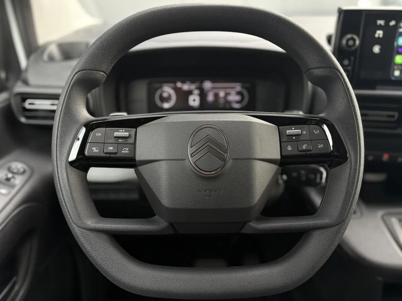 Vue rapprochée du volant multifonctions noir du Citroën Berlingo 2025 avec tableau de bord numérique en arrière-plan.