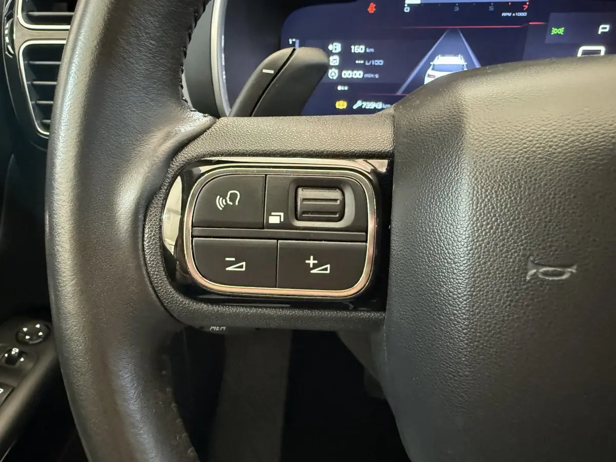 Gros plan sur les commandes gauche du volant cuir noir du Citroën C5 Aircross 2020, tableau de bord numérique en arrière-plan.