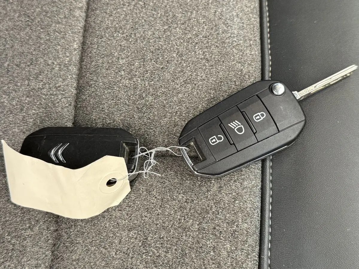 Clé de voiture CITROEN posée sur un siège gris, avec télécommande noire et étiquette attachée.