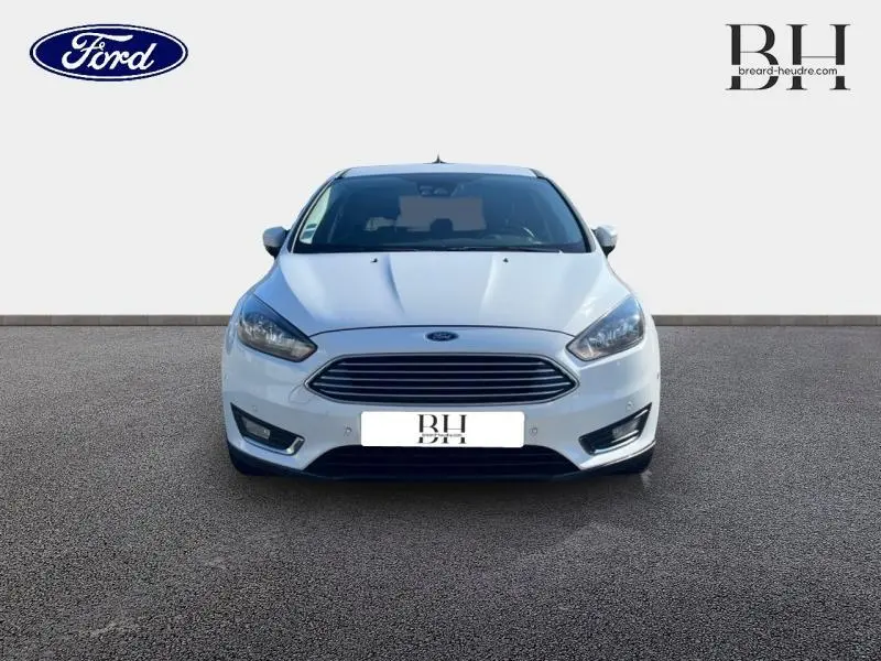 Vue frontale d'une Ford Focus blanc glacier 2017 avec calandre chromée et phares halogènes allumés.