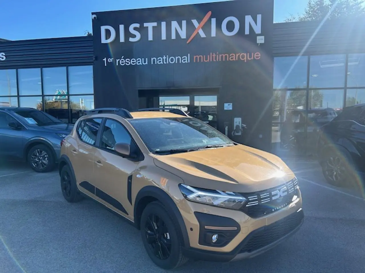 Dacia Sandero III Stepway beige Safari vue 3/4 avant droit, avec barres de toit et jantes noires.