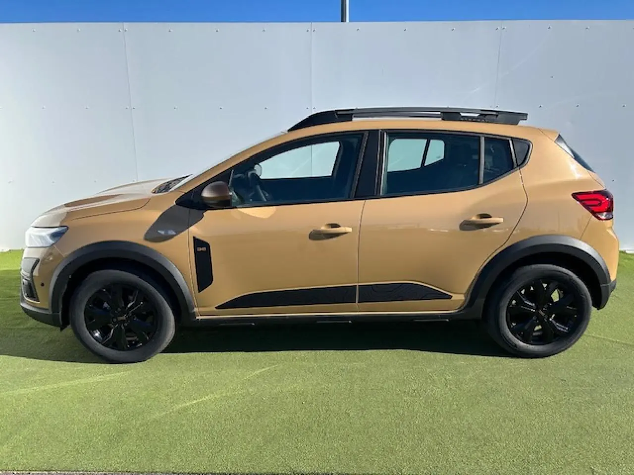 Profil droit de la Dacia Sandero Stepway beige Safari 2025 avec barres de toit et jantes noires.