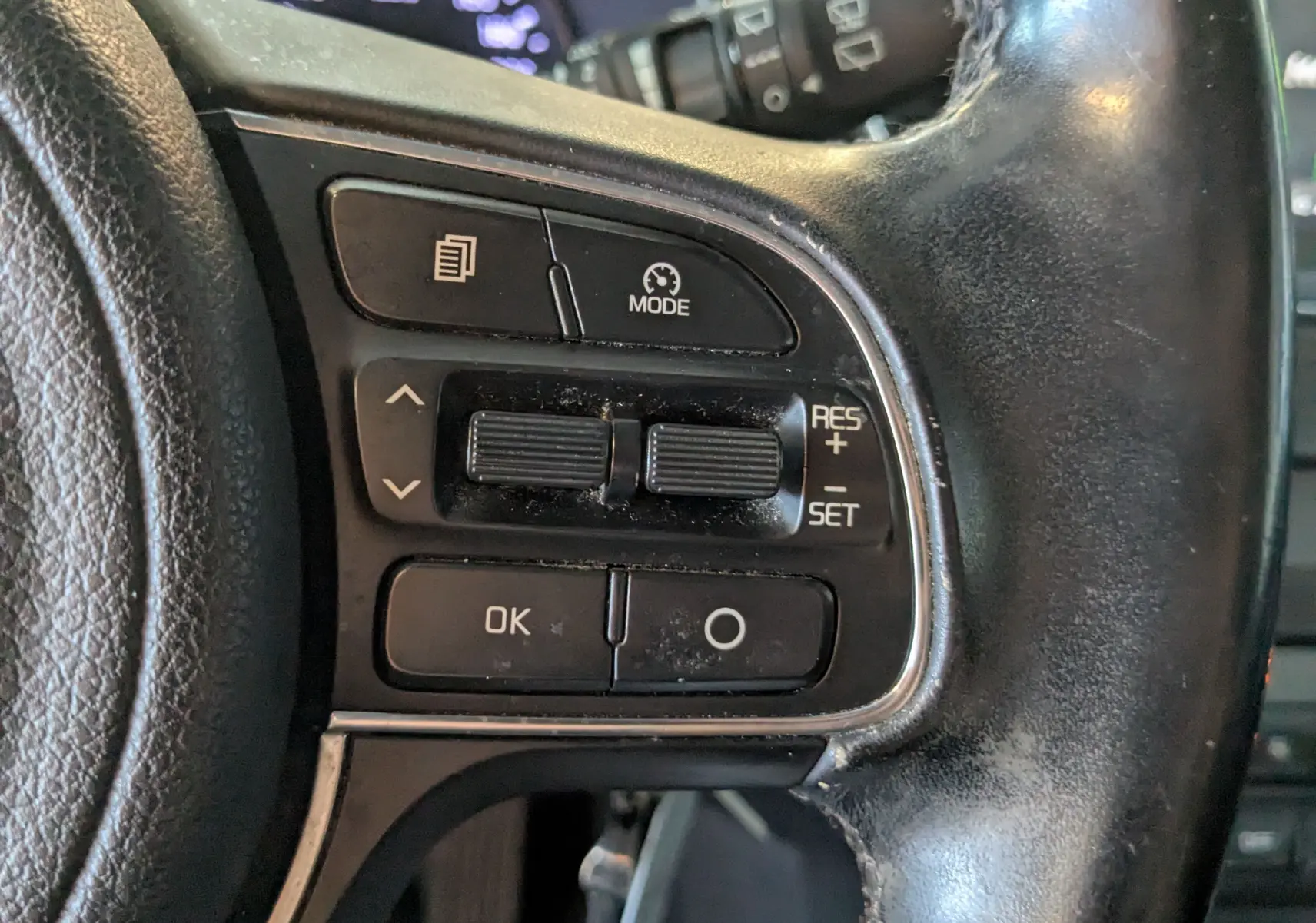 Gros plan sur les commandes de régulateur de vitesse au volant noir d’un KIA Sportage gris 2016.