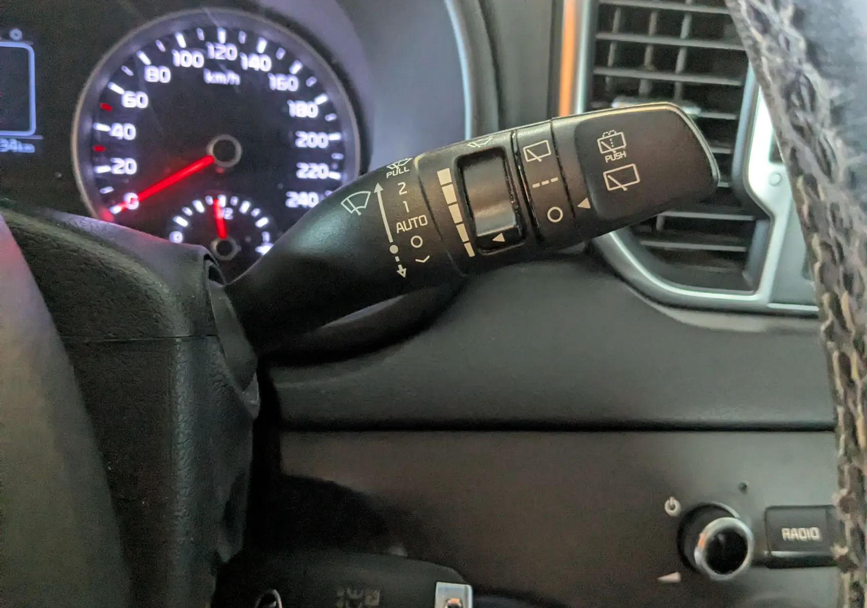 Gros plan sur la commande d’essuie-glace à droite du volant dans l’habitacle gris du Kia Sportage 2016.