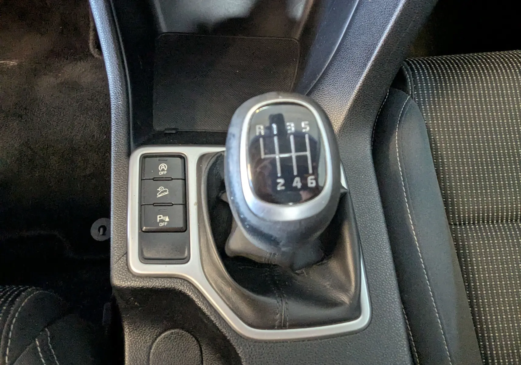 Gros plan sur le levier de vitesses manuel noir et argenté du KIA Sportage gris, avec boutons de contrôle à gauche.