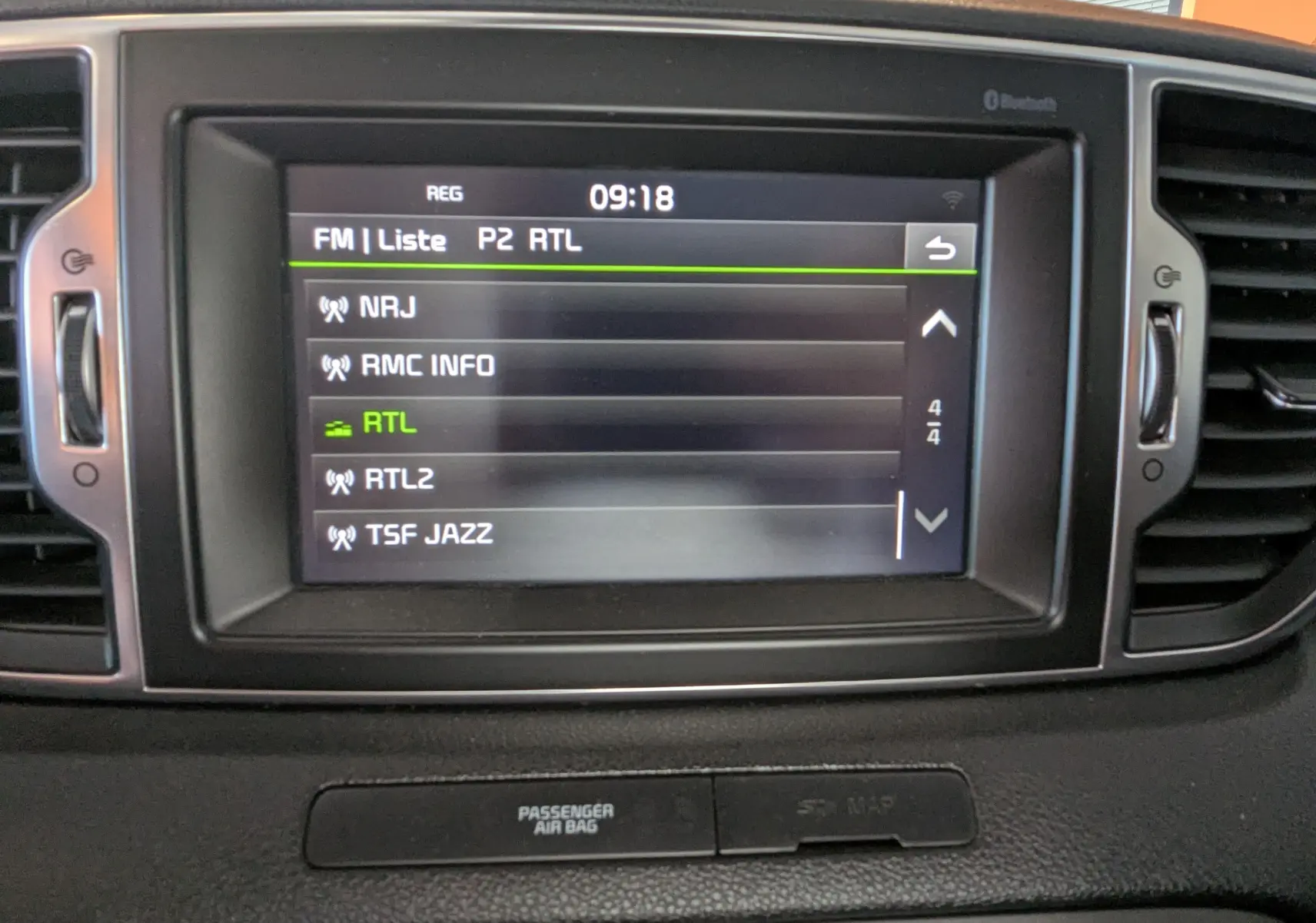 Écran central tactile du tableau de bord du Kia Sportage gris 2016 affichant la liste des stations radio FM.