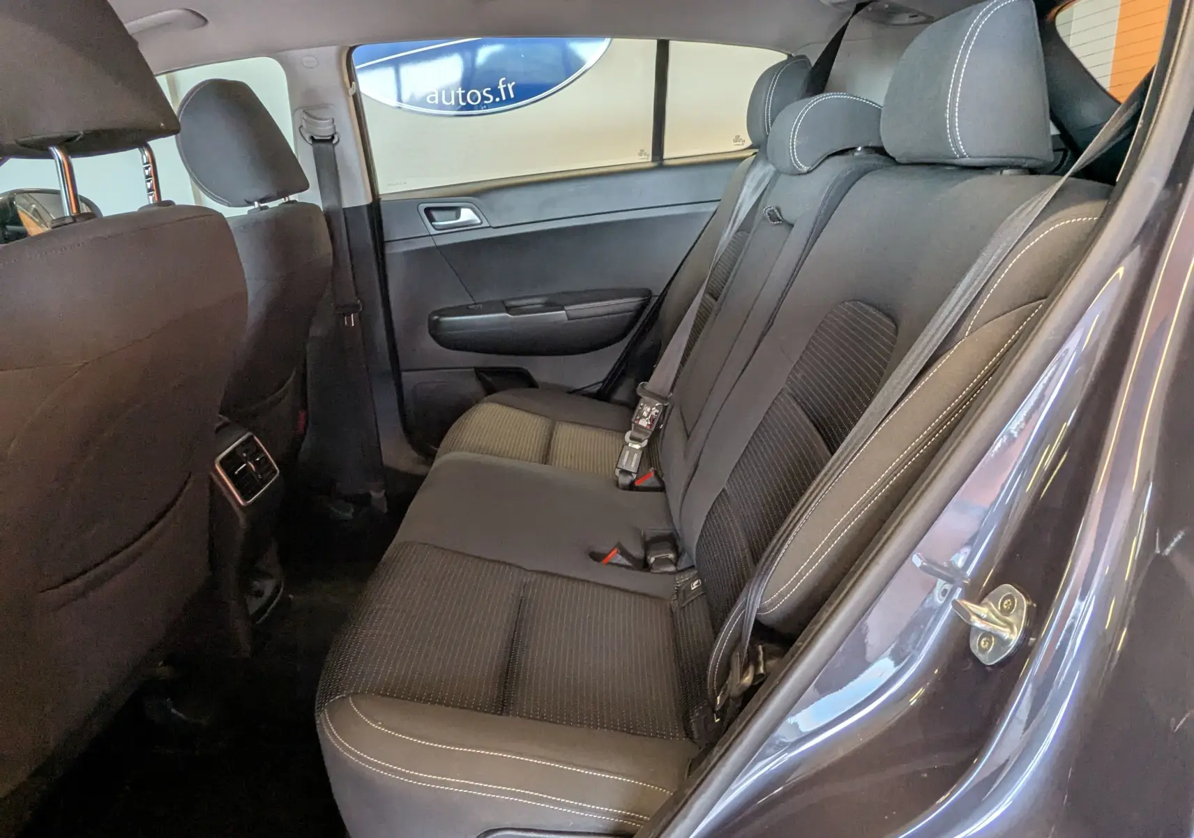 Vue intérieure côté droit des sièges arrière gris foncé du Kia Sportage 2016 avec ceinture de sécurité et appuie-têtes visibles.