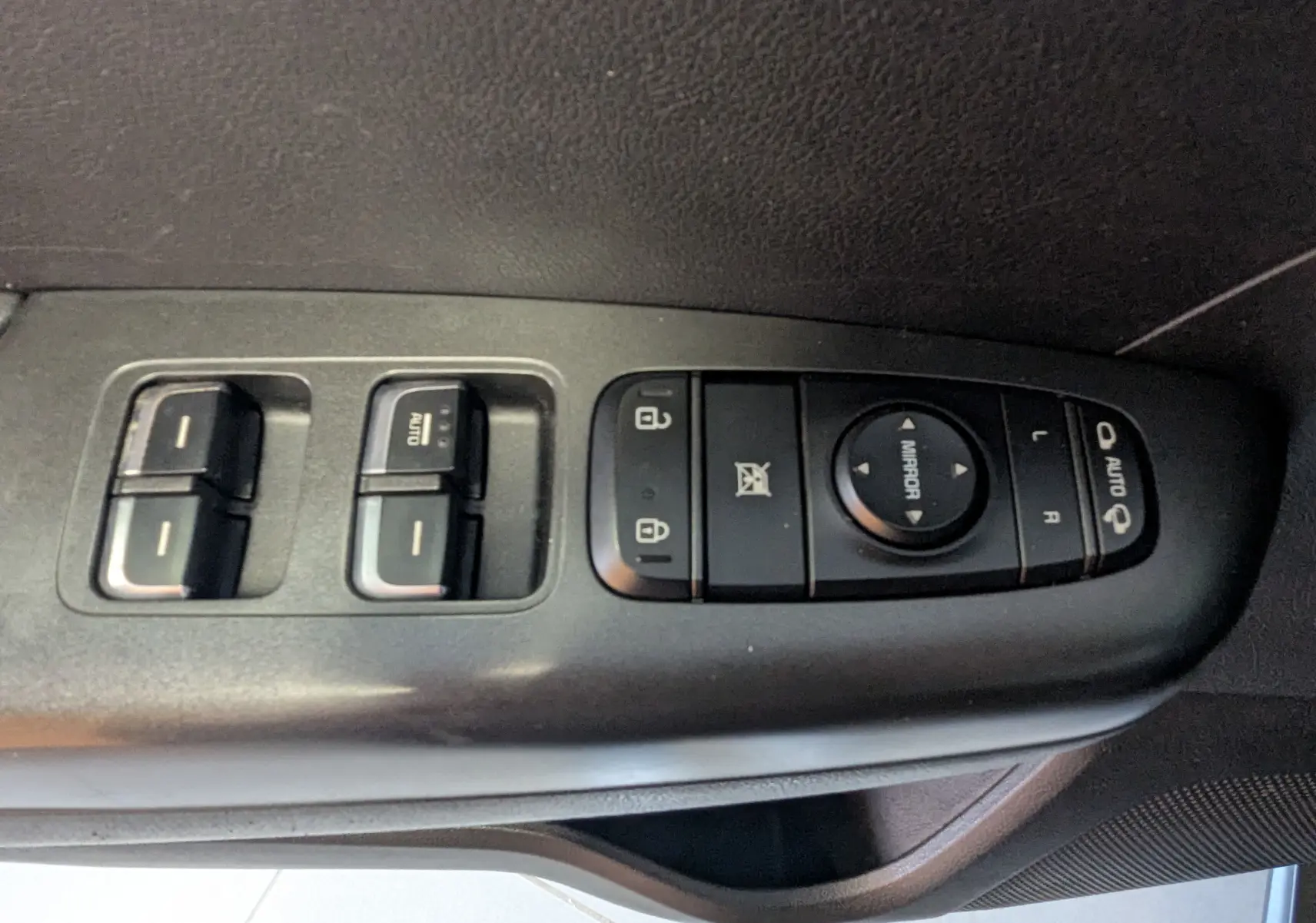 Vue rapprochée des commandes de lève-vitres et réglage des rétroviseurs sur la porte côté conducteur d'un KIA Sportage gris 2016.