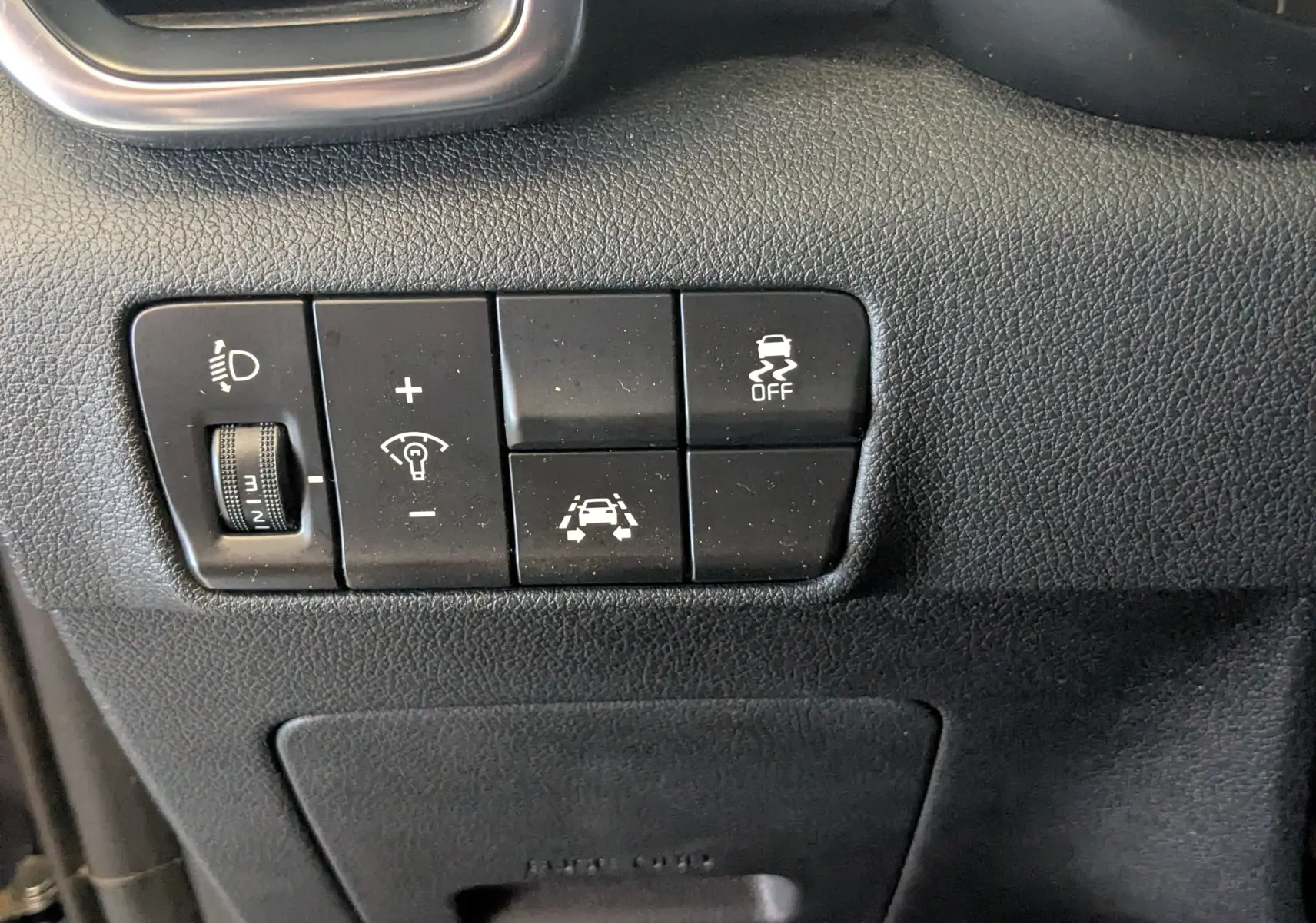 Gros plan sur les commandes noires du tableau de bord côté gauche du Kia Sportage gris, avec réglage phares et aides à la conduite.