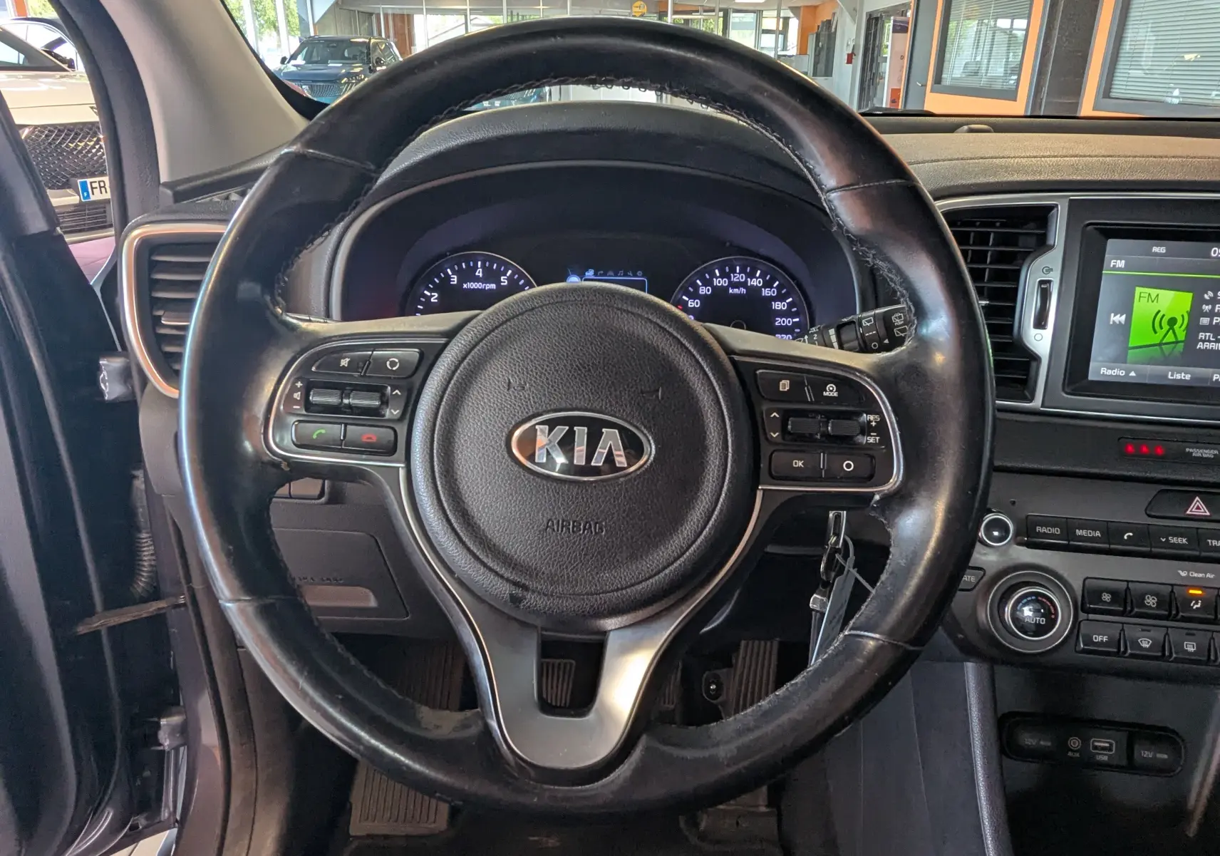 Vue intérieure centrée sur le volant noir du Kia Sportage 2016 avec tableau de bord et écran multimédia visibles.