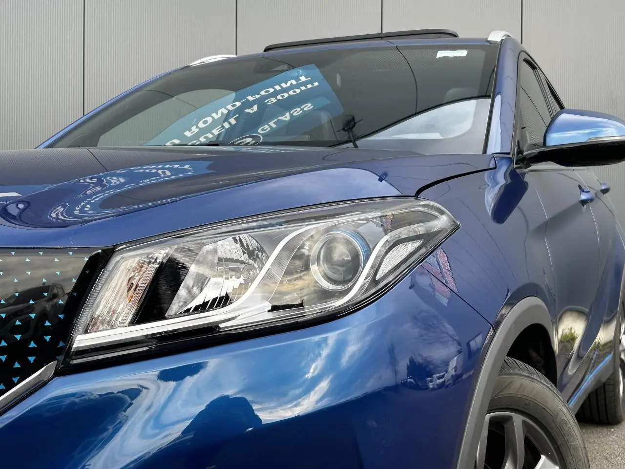 Gros plan sur le phare avant droit bleu du SUV électrique SERES 3 163 Luxury avec calandre noire à motifs bleus.