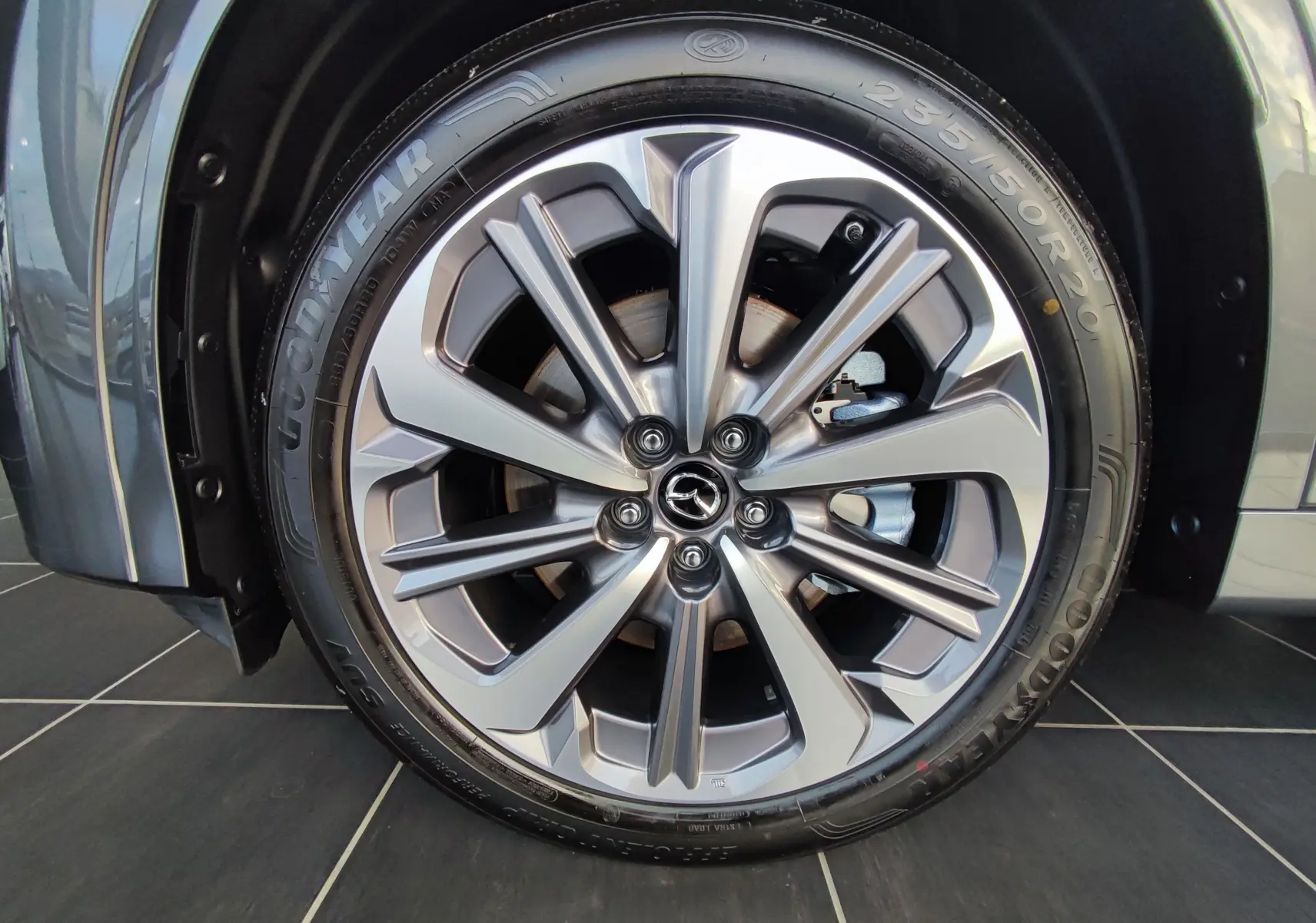 Gros plan sur la jante alliage 20 pouces du Mazda CX-80 gris foncé, mettant en valeur le logo Mazda central.