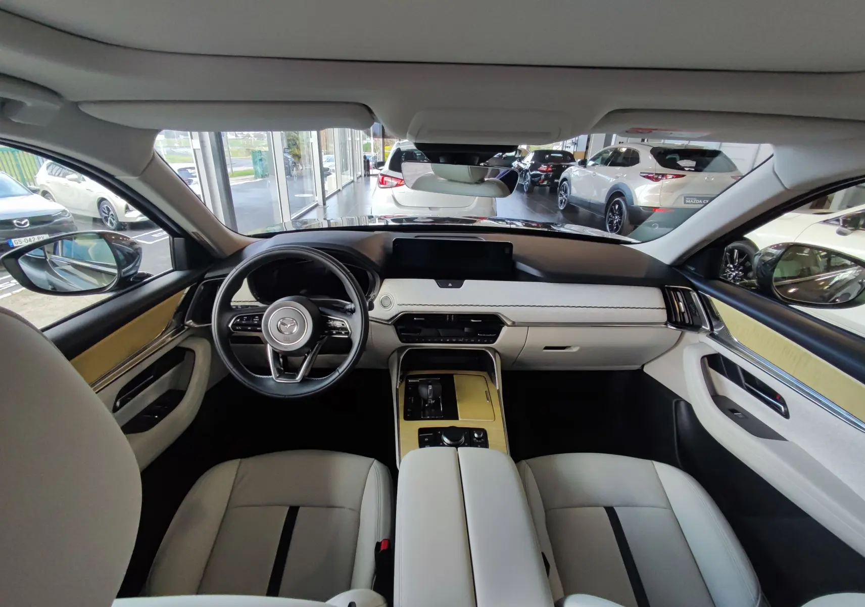 Vue intérieure avant du Mazda CX-80 2024 avec tableau de bord clair et finitions bois sur console centrale.