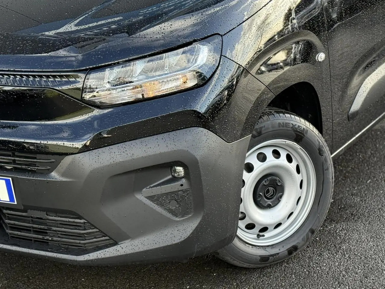 Gros plan sur l'avant droit noir perla du Citroën Berlingo Van 2025 avec phare et jante tôle grise visible sous la pluie.