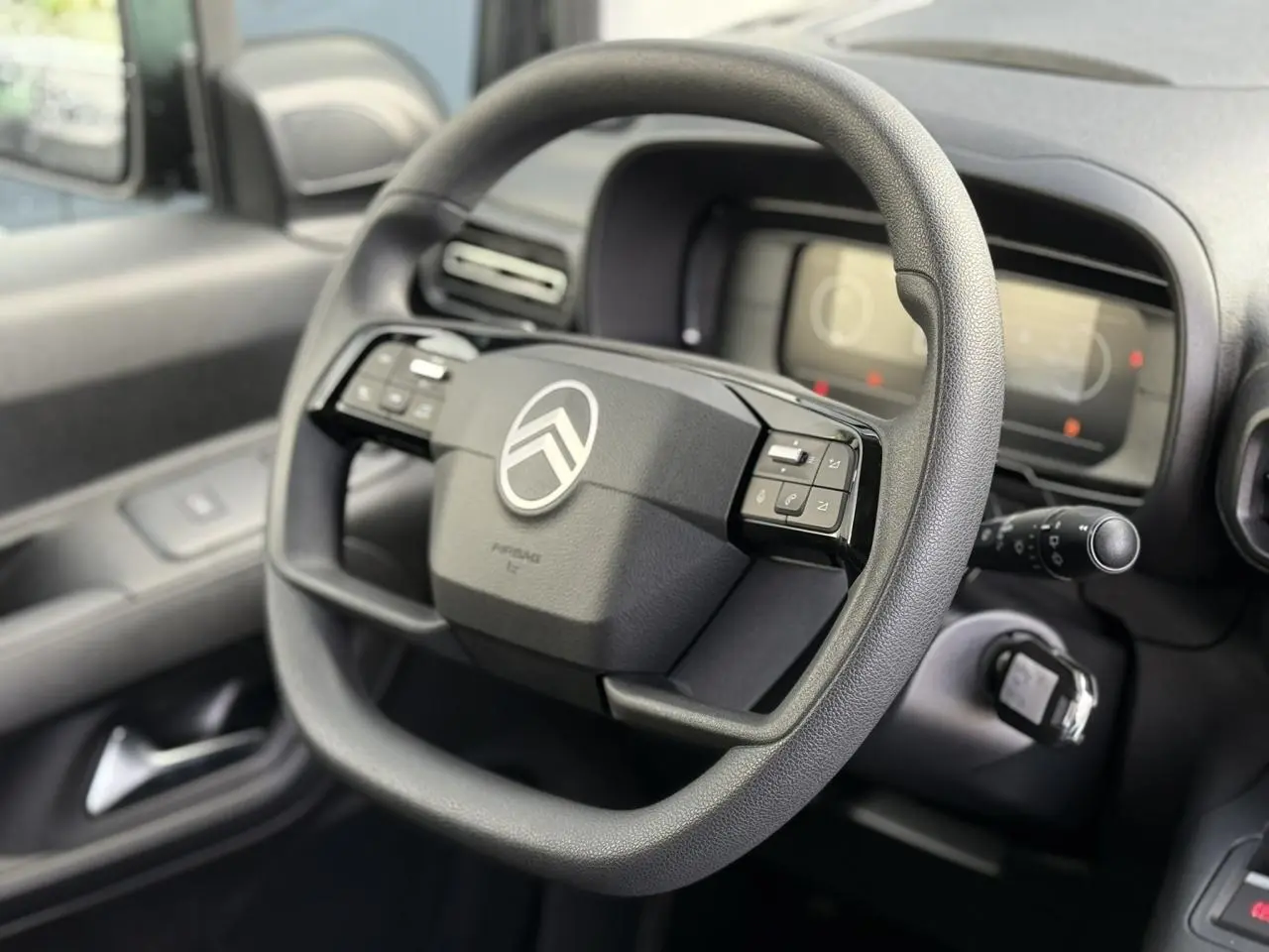 Volant multifonctions noir de Citroën Berlingo 2025, vue rapprochée côté conducteur avec tableau de bord numérique flou.