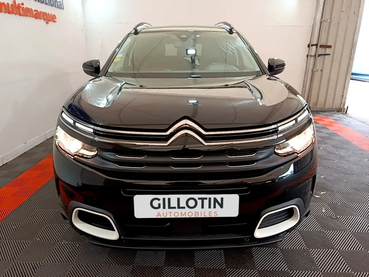 Vue frontale d'un Citroën C5 Aircross noir 2020 avec calandre distinctive et phares allumés dans un showroom.