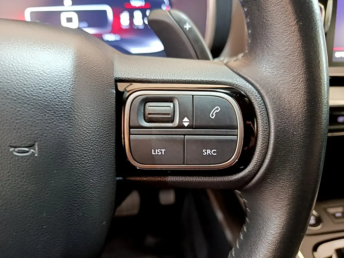 Gros plan sur les commandes gauche du volant cuir noir du Citroën C5 Aircross 2020 avec affichage digital en arrière-plan.