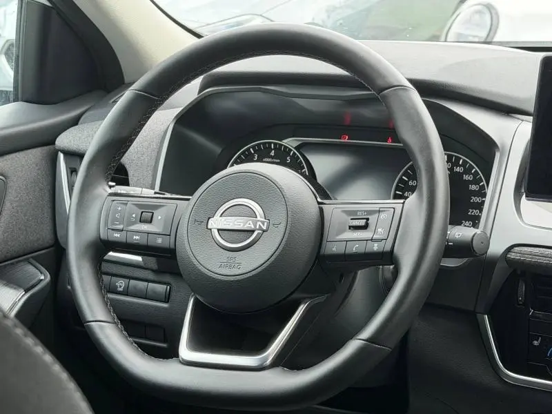 Vue rapprochée du volant cuir multifonction noir du Nissan Qashqai 2025 avec tableau de bord numérique en arrière-plan.