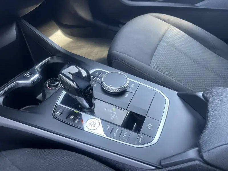 Gros plan sur la console centrale noire de la BMW Série 1 116dA avec levier de vitesses automatique et accoudoir tissu anthracite.