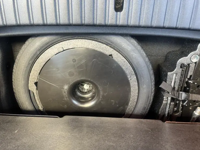 Gros plan sur la roue de secours et le compartiment de rangement dans le coffre d'une BMW Série 1 noire 116dA.