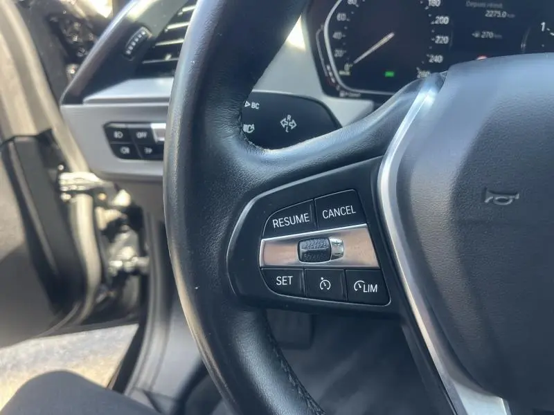 Gros plan sur le volant cuir noir de la BMW Série 1 116dA 2020, montrant les commandes multifonctions côté gauche.