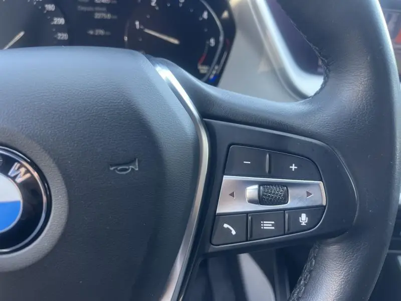 Gros plan sur le volant cuir noir de la BMW Série 1 116dA 2020, avec commandes multifonctions et logo central visible.