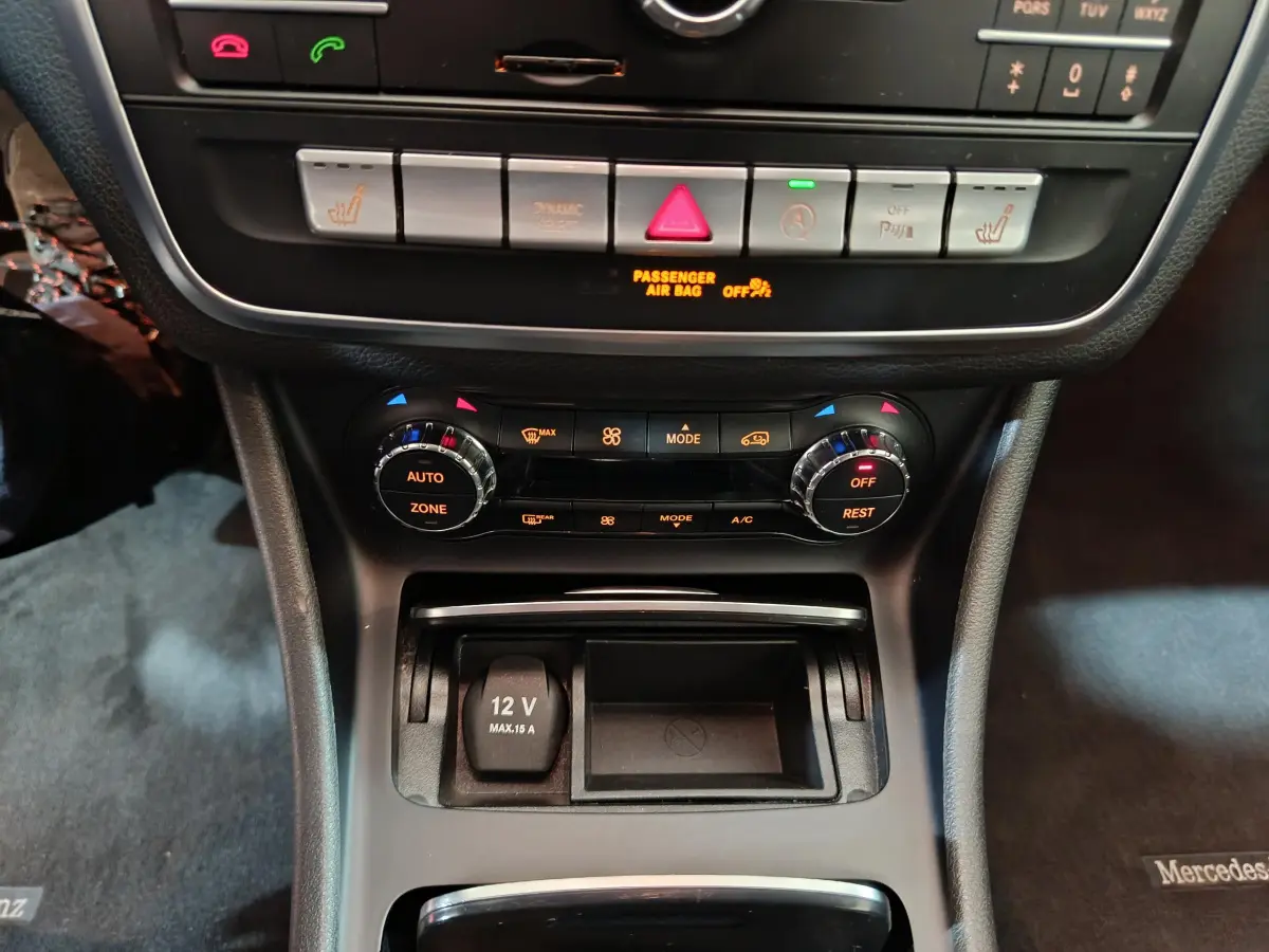 Vue rapprochée de la console centrale noire du Mercedes GLA 200 d, avec commandes climatisation et prise 12V visible.