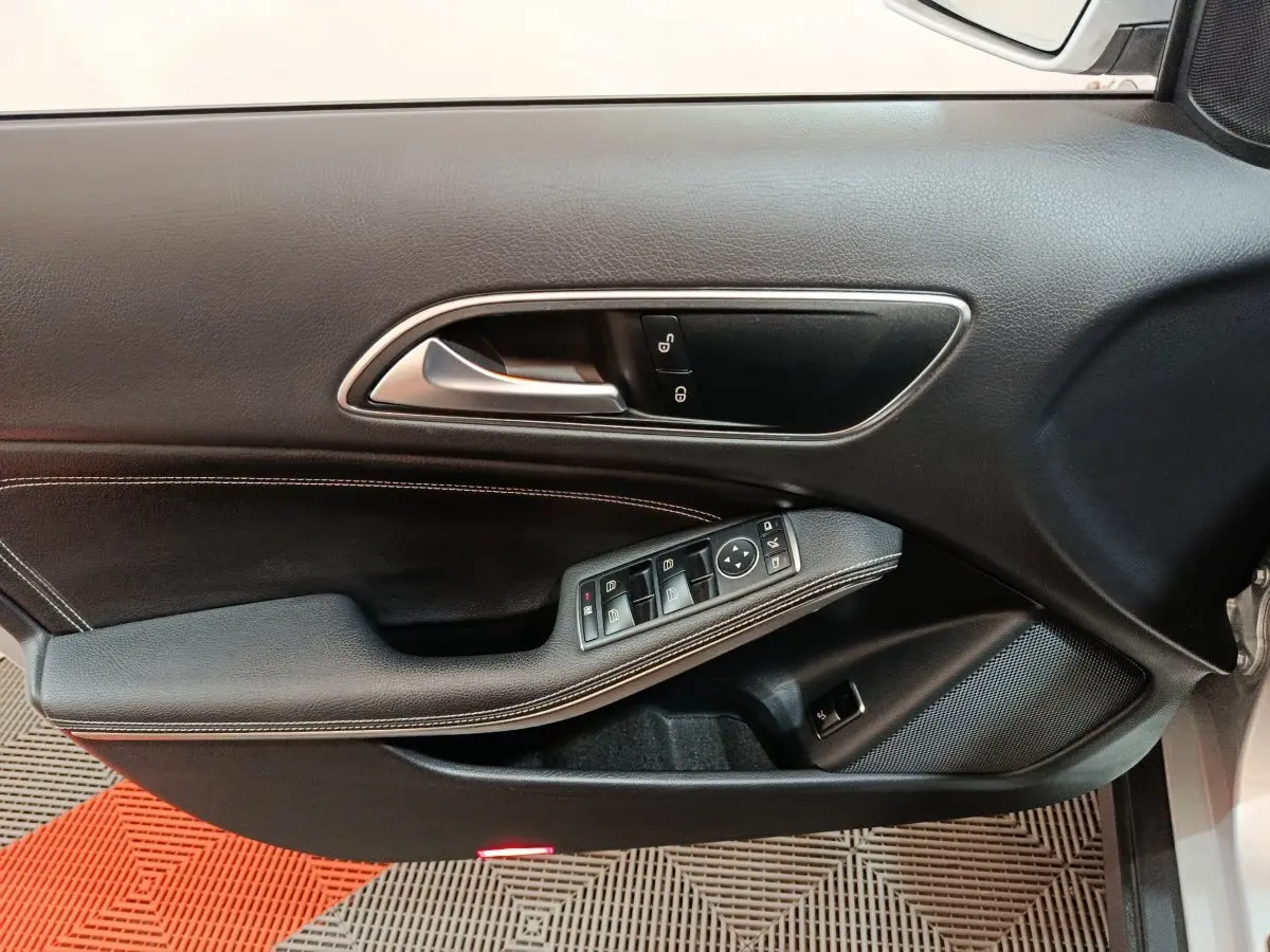 Gros plan sur la porte côté conducteur du Mercedes GLA 200 d gris clair, montrant les commandes de vitres et la poignée intérieure chrome.