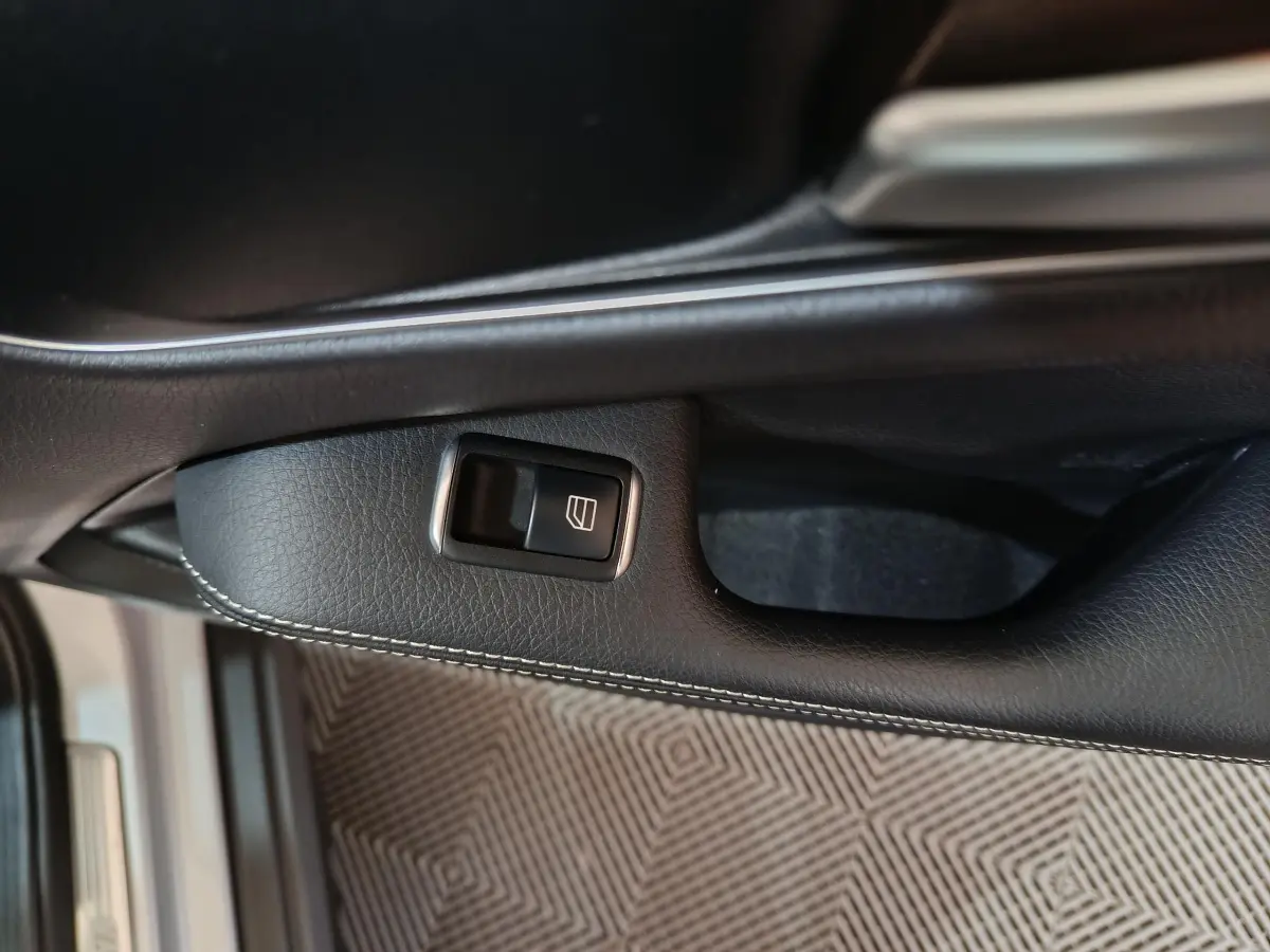 Gros plan sur la commande de lève-vitre côté conducteur en cuir noir avec surpiqûres, Mercedes GLA 200 d gris clair.