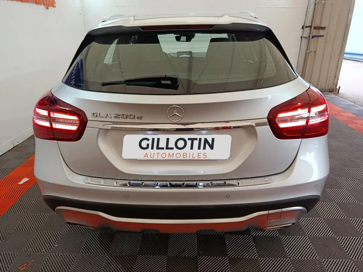 Vue arrière d'un Mercedes GLA 200 d gris clair avec feux LED et logo Mercedes visible sur un sol à damier noir et orange.