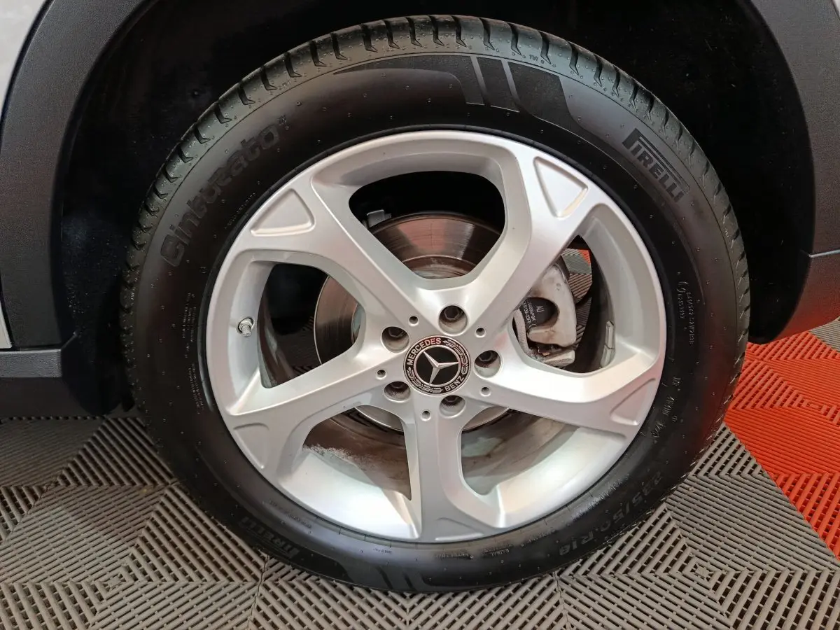 Gros plan sur la roue arrière droite d'un Mercedes GLA 200 d gris clair, avec passage de roue noir et sol en damier rouge et gris.