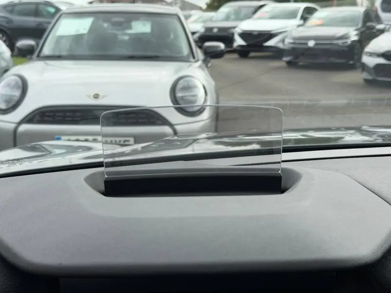 Vue depuis l'intérieur du tableau de bord avec affichage tête haute, sur une Citroën C4 X 2024 gris Platinium en arrière-plan flou.