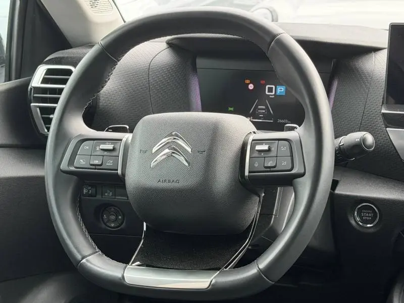 Vue rapprochée du volant noir du Citroën C4 X 2024 avec commandes intégrées et tableau de bord numérique en arrière-plan.