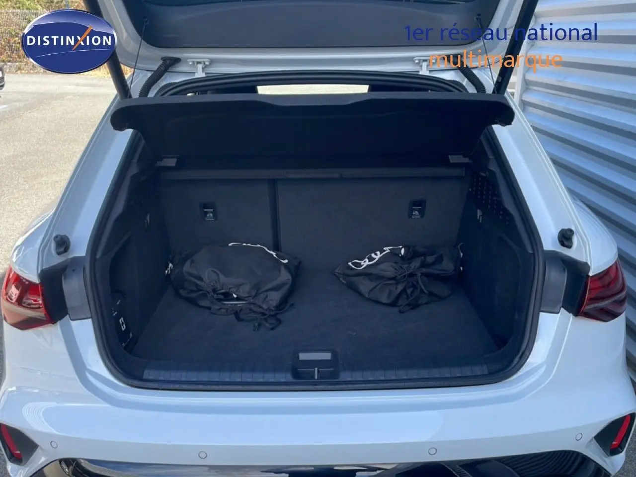 Coffre ouvert vu de l'arrière d'une Audi A3 Sportback blanc Ibis avec deux sacs noirs à l'intérieur.