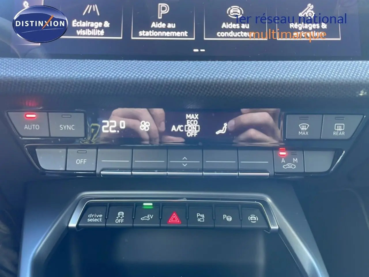 Vue rapprochée de la console centrale de l'Audi A3 Sportback blanche, avec commandes climatisation et aides à la conduite.