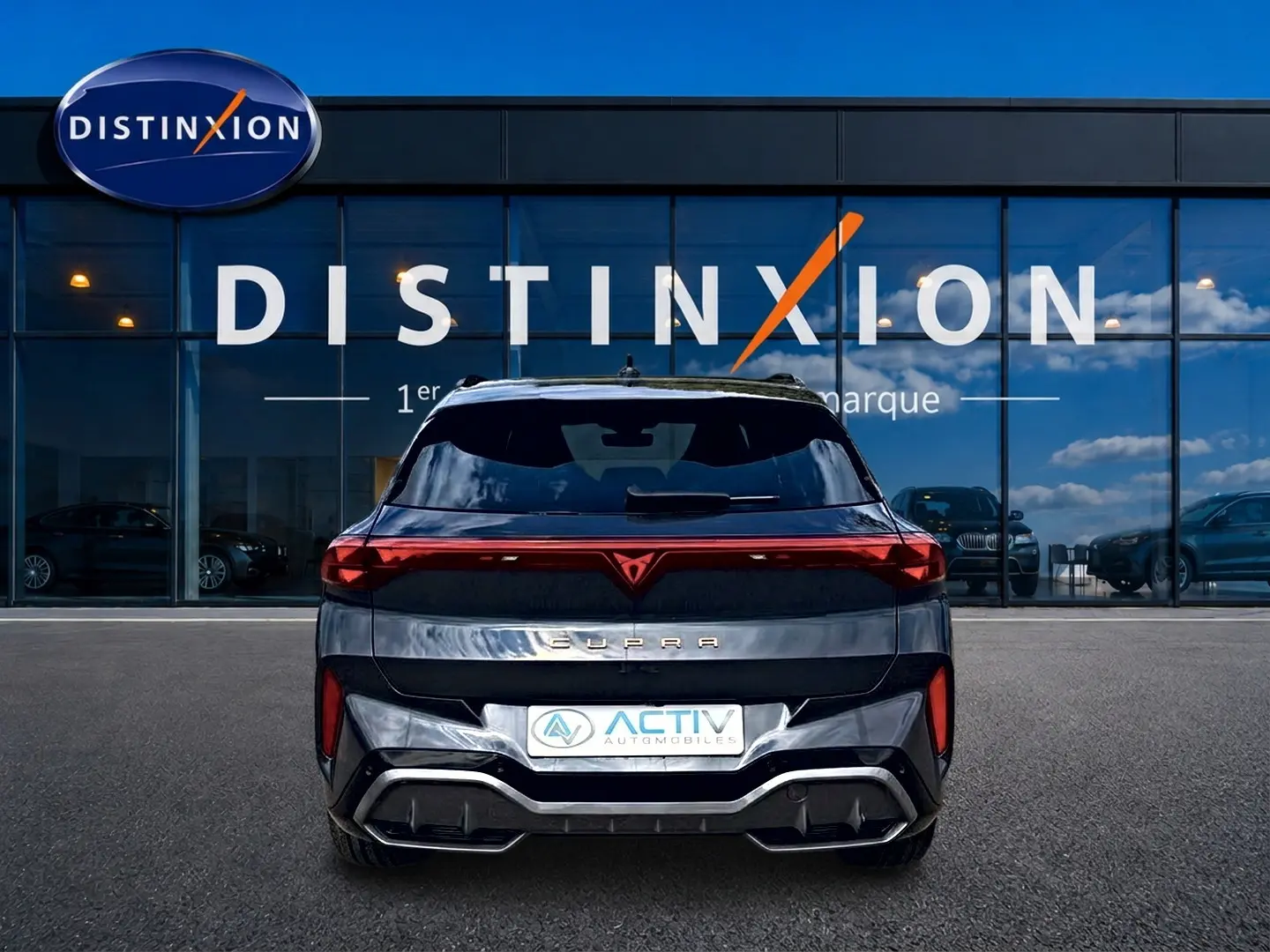 Vue arrière d'un CUPRA TERRAMAR gris timanfaya avec feux LED reliés et diffuseur noir, devant une vitrine Distinxion.
