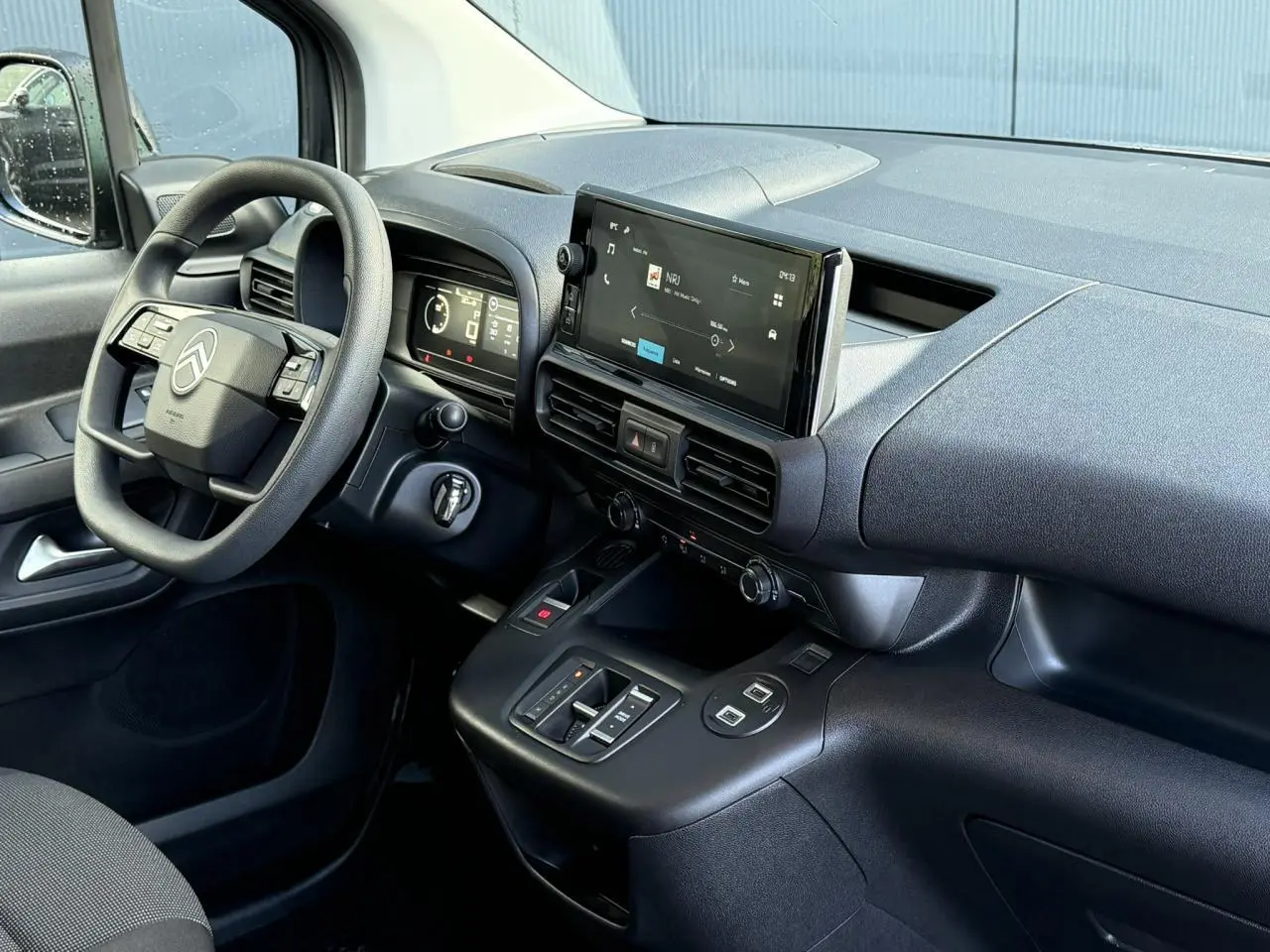 Intérieur côté conducteur du Citroën Berlingo 2025, tableau de bord noir avec écran tactile central et volant multifonctions.