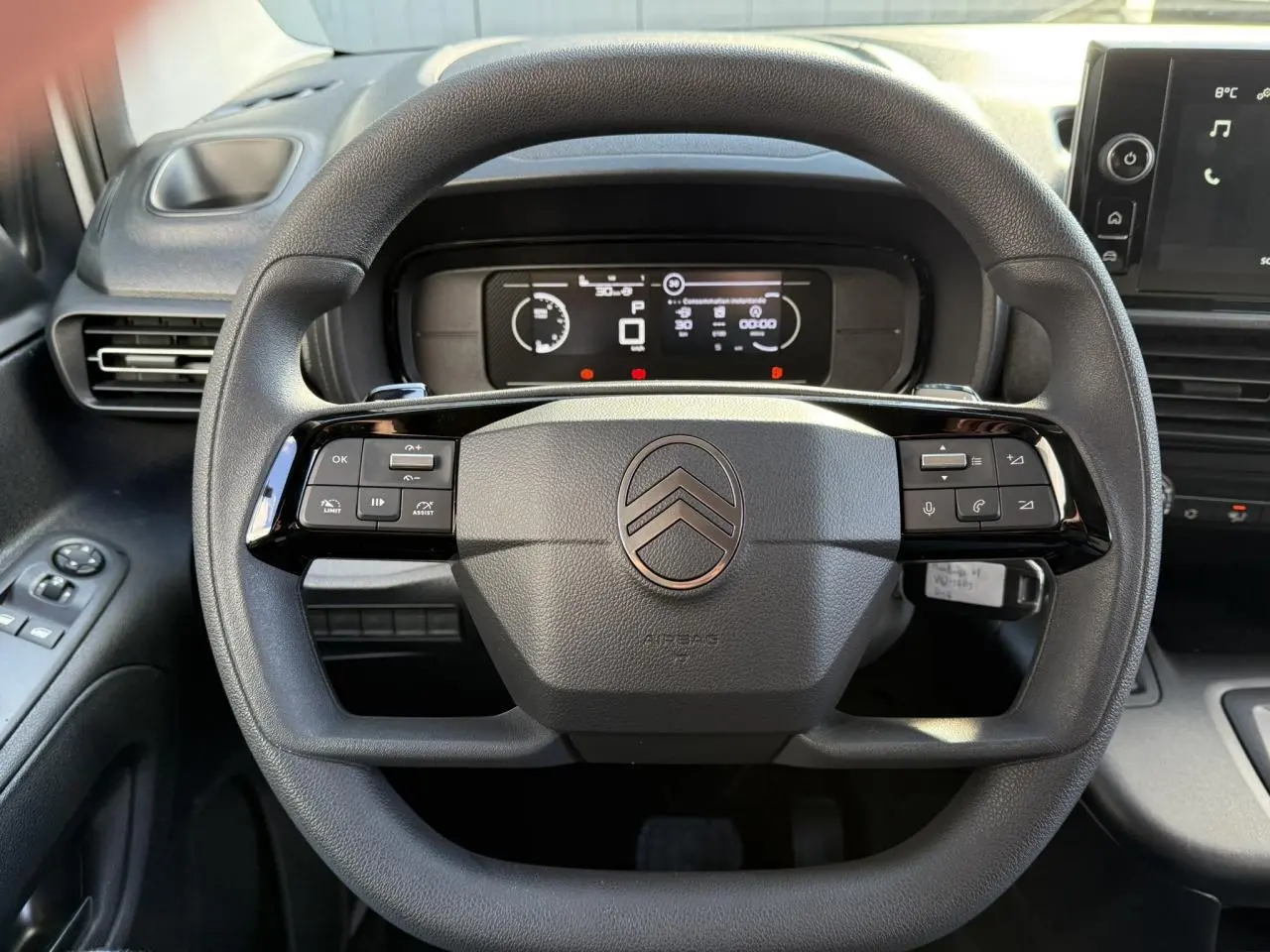 Vue rapprochée du volant multifonctions noir du Citroën Berlingo 2025 avec tableau de bord numérique en arrière-plan.