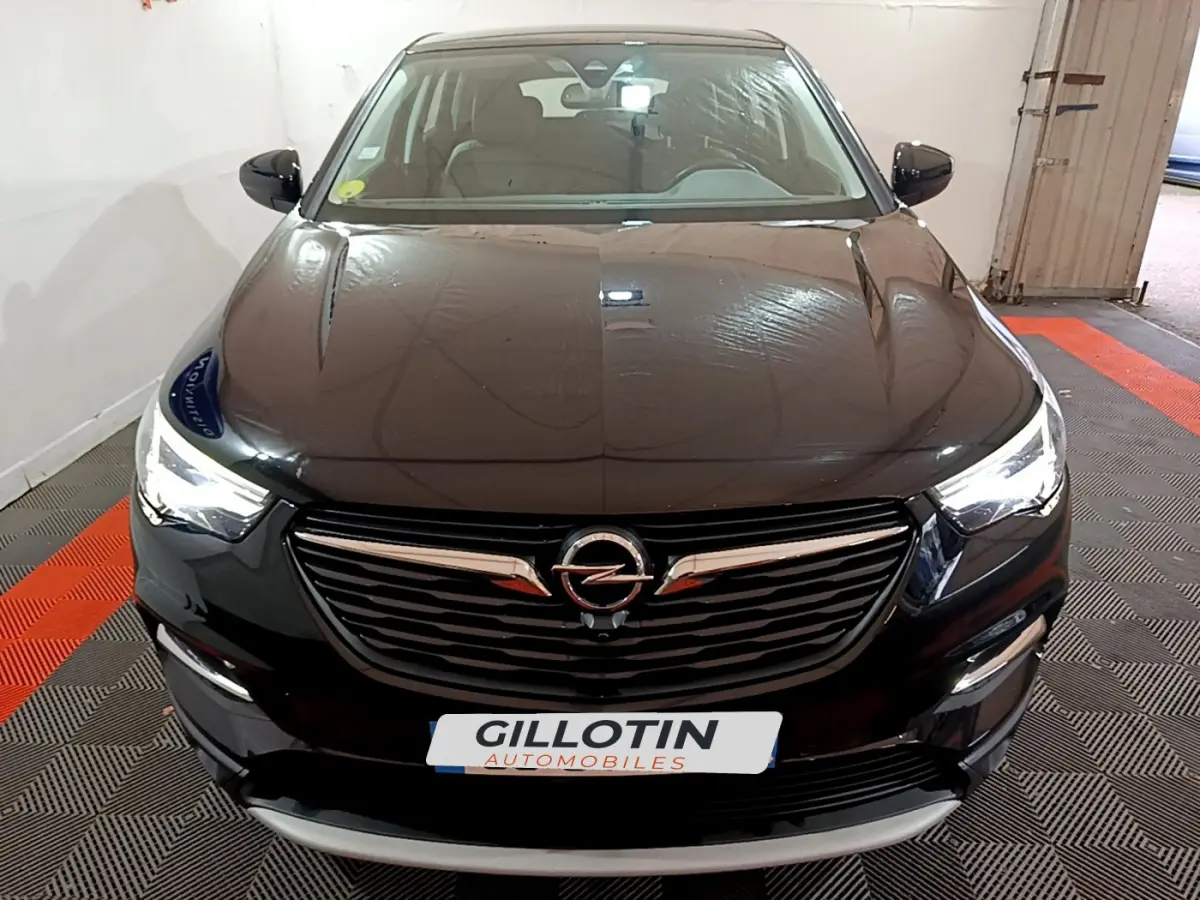 Vue frontale d'un Opel Grandland X noir avec phares LED allumés et calandre chromée dans un garage.