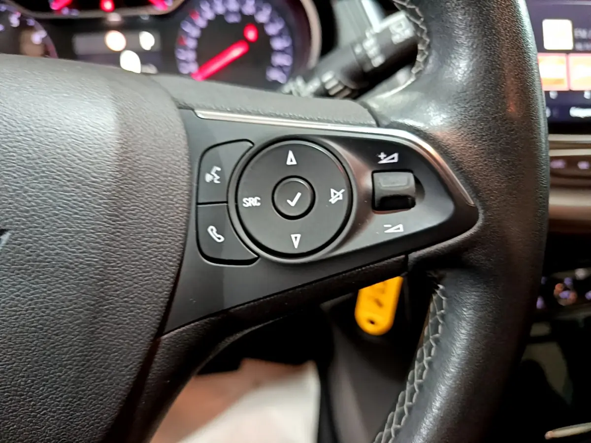 Gros plan sur les commandes gauche du volant cuir noir de l'Opel Grandland X 2021 avec tableau de bord en arrière-plan flou.