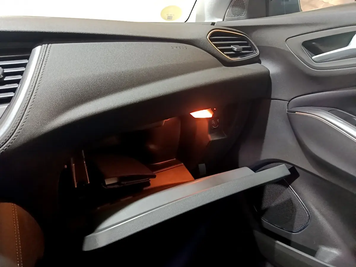 Intérieur de l'Opel Grandland X 2021, vue côté passager sur boîte à gants ouverte avec éclairage intérieur chaud.
