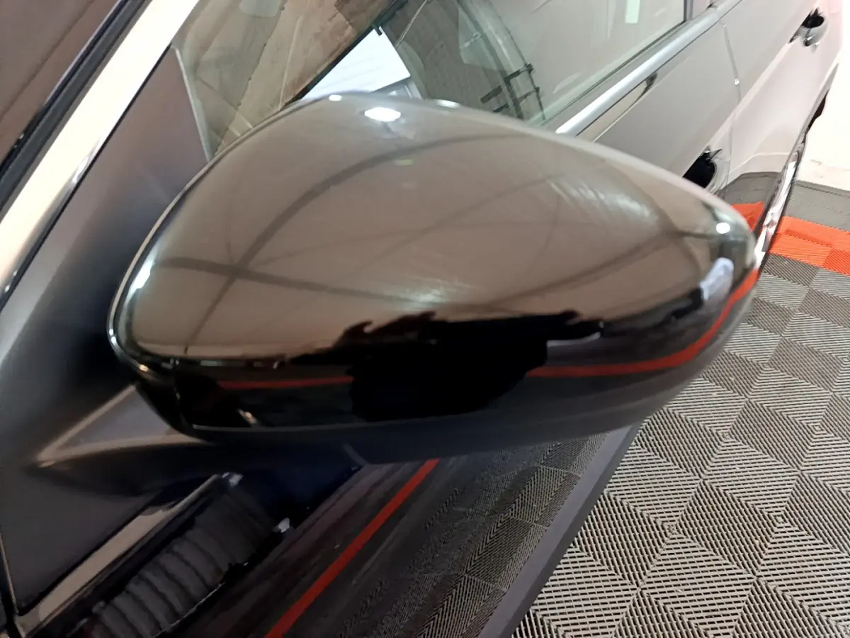 Rétroviseur noir brillant côté gauche en gros plan sur Opel Grandland X noir, reflet de l'environnement intérieur visible.