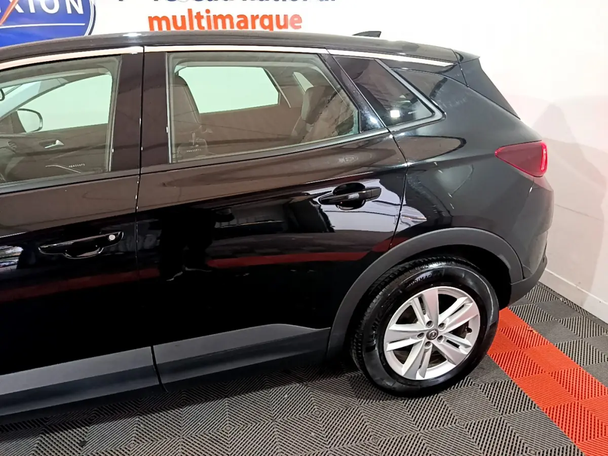 Vue latérale côté droit d'un Opel Grandland X noir avec jantes alliage et feux arrière LED visibles en intérieur showroom.